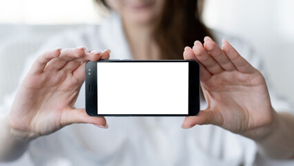 Digital mockup. Mobile selfie. Online connection. Unrecognizable defocused woman holding smartphone with blank screen in light room interior.