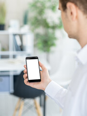 Virtual conference. Digital mockup. Office work. Unrecognizable man holding smartphone with blank screen in light room interior.