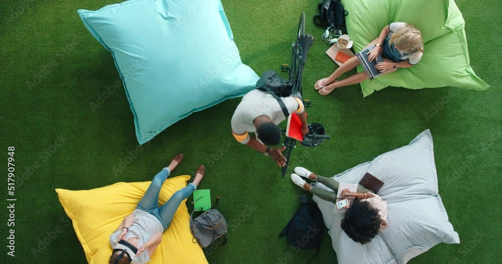 Poster above view of creative businesspeople relaxing and working on bean bags in an informal office setup.