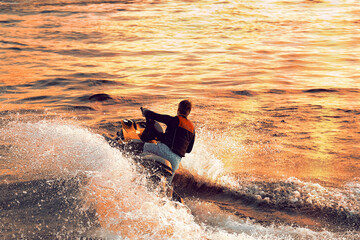 A guy on a jet ski swims at high speed across the sea. A man rides a jet ski in the sun at sunset. Splashes of water in different directions.