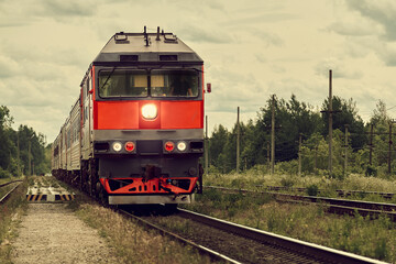 Russian passenger train rides on rails through the forest. Soviet diesel locomotive pulling passenger cars.