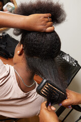 femme noire africaine aux cheveux frisés et longs faisant un lissage chez une coiffeuse ave cun...