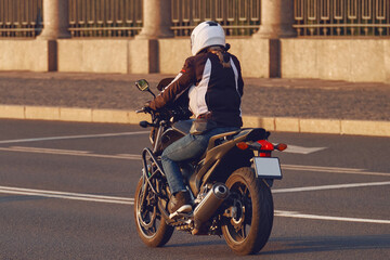 A girl in a helmet rides a motorcycle in the evening city. Young woman motorcyclist travels on a...