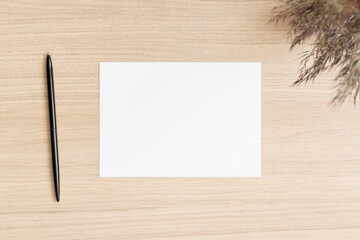White invitation card mockup with a dry flower on the wooden table. Workspace concept. 5x7 ratio, similar to A6, A5.