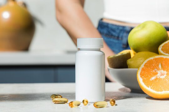  Mockup of a white plastic jar with vitamin D or fish oil capsules on the kitchen table. Nutritional supplements.