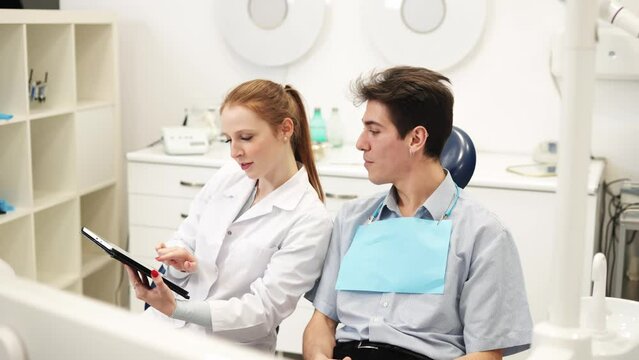 Young friendly female dentist and male patient discussing dental procedure costs