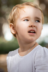 Toddler girl looking away in blurred park.