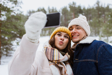 season, technology and leisure concept - happy couple with smartphone taking selfie in winter park