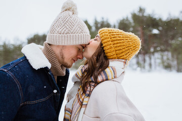 people, love and leisure concept - happy woman kissing man to forehead in winter forest