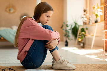 Depressed teen girl sitting on floor and hugging her knees, suffering from cyber bullying, being...