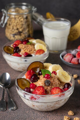 Granola crispy muesli with natural yogurt, frozen berries, fruit and nuts in two glass bowls on brown background