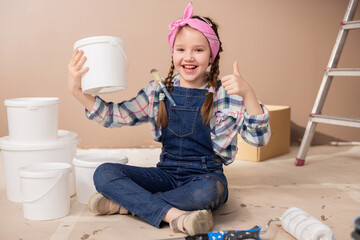 Smiling happy little daughter helps parents painting living room walls. The child sits on the floor...