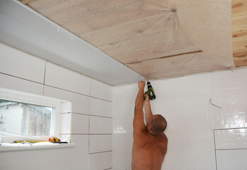 Contractor installing white PVC ceiling boards with screw gun in the new house bathroom. PVC ceiling boards installation.