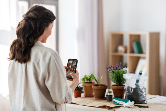 people, gardening and housework concept - happy woman with smartphone photographing pot flowers at home