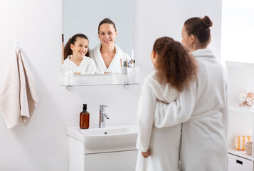 beauty, hygiene, morning and people concept - happy smiling mother and daughter looking to mirror...