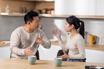 Asian couple arguing while drinking coffee at kitchen