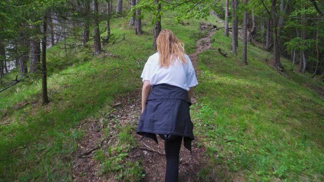 Female Hiker Climbing On An Uphill Trail With Trees In The Mountain. - rear follow