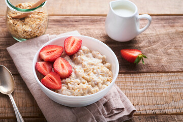 Oatmeal. Bowl of oatmeal porridge with strawberry, almond and milk on old wooden dark table background. Top view in flat lay style. Natural ingredients. Hot and healthy breakfast and diet food.