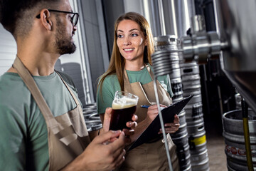 Man and woman working in craft brewery examining quality of the beer.