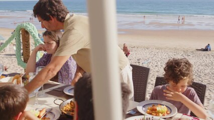 4K SlowMo - family and friends gathered for lunch enjoying a delicious paella in a bar on the beach - happy little kids playing around the table after eating, eating dessert and ice cream - Powered by Adobe