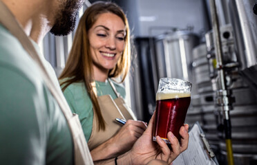 Man and woman working in craft brewery examining quality of the beer.