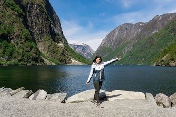 Fototapeta na wymiar Young tourist woman at the foot of the fjord surrounded by high mountains in Gudvangen - Norway