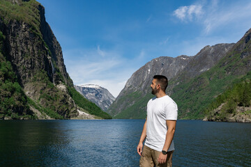 Fototapeta na wymiar Young male tourist in the foreground and behind him the high mountains and the fjord, in Gudvangen - Norway