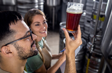 Man and woman working in craft brewery examining quality of the beer.