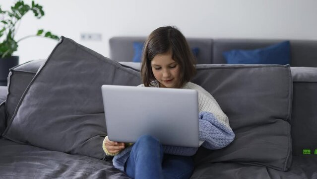 Little school kid girl use laptop computer sitting on sofa