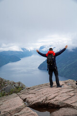 Unrecognizable young man raising his hands with the Lysefjord fjord in the background - concept of success and self-improvement