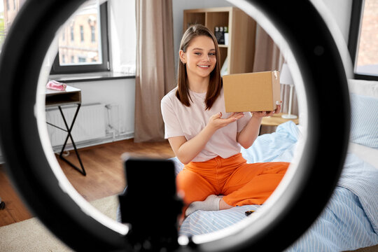 blogging, technology and people concept - happy smiling girl blogger with ring light and smartphone unpacking parcel box at home