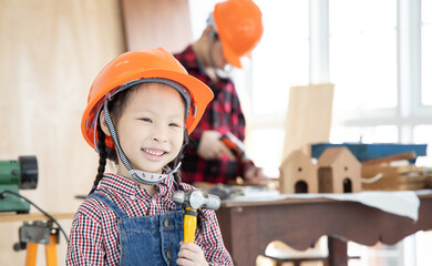 Asian little girl holding a hammer during playing in carpenter workshop