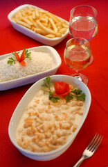 Shrimp in white cheese sauce in white bowl on red tablecloth.
