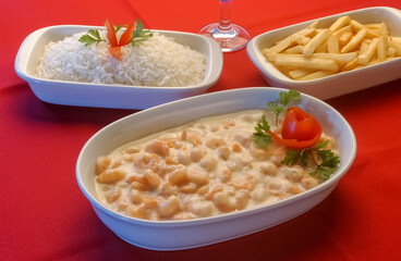 Shrimp in white cheese sauce in white bowl on red tablecloth.