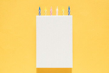 White cardboard vertical poster with cake candles on top on a bright yellow background. Happy birthday, anniversary, anniversary greeting card. Mock up for design, logo or text insert template.