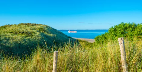 Keuken foto achterwand Noordzee, Nederland Groene met gras begroeide duinen langs een zandstrand en een zee onder een blauwe lucht in fel zonlicht in de zomer, Walcheren, Zeeland, Nederland, juli 2022