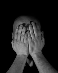 Fototapeta premium a man on a black background covering his face with his hands with one light source