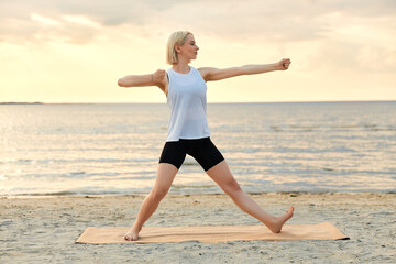 Fototapeta na wymiar fitness, sport, and healthy lifestyle concept - woman doing yoga archer pose on beach over sunset