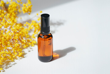 Amber pump bottle with serum, tonic or essential oil with yellow flowers. White background with daylight. Beauty concept for face and body care