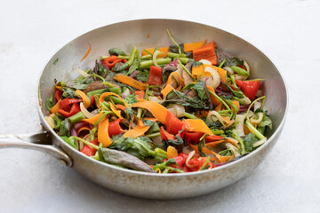 STEEL FRYING PAN OF FRESHLY COOKED COLOURFUL ORGANIC VEG ON SILVER SURFACE 