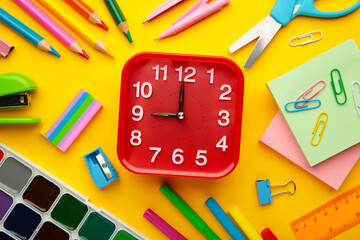 Alarm clock, paint, pencils and scissors. School accessories on a yellow background. Back to school concept.