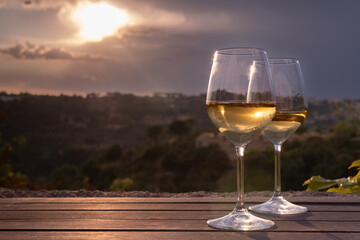 Two elegant glasses of white wine on a table with countryside in the background, at sunset