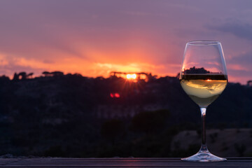 An elegant glass of white wine with the sun setting and dark countryside in the background
