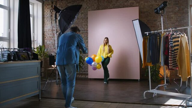 Young photographer taking picures of model with balloons, backstage of photoshooting in studio.