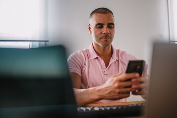 Focused business man entrepreneur with smartphone. Male professional using cell phone sitting at home office desk. Busy worker freelancer working on modern tech notebook device.