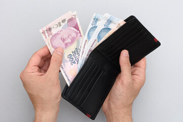 Male hand holding wallet with Turkish lira. Gray background.
