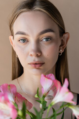 Fototapeta premium portrait of young woman with clean skin and natural makeup looking at camera isolated on beige.