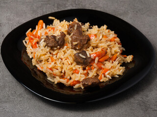 traditional Uzbek pilaf on a black plate on a gray background