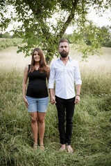 pretty young pregnant woman with black shirt is standing with her boyfriend in a high meadow and they are happy and full of anticipation for the baby