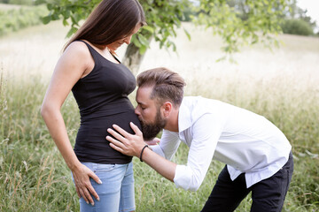 Obraz premium pretty young pregnant woman with black shirt is standing with her boyfriend in a high meadow and they are happy and full of anticipation for the baby